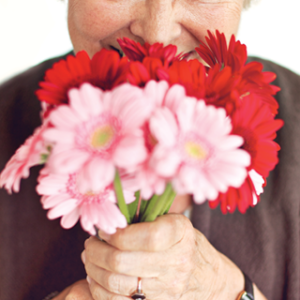 cheerful older woman holding bouquet of flowers up to her nose