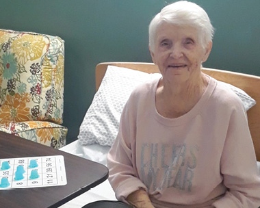 senior woman with grey hair and baby pink sweater sitting at table playing bingo