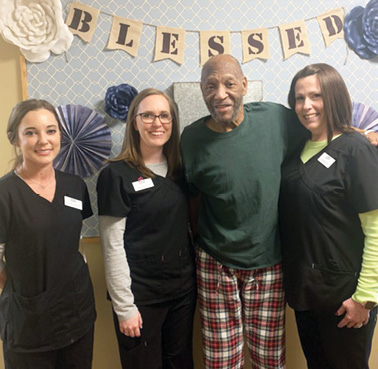 Resident William S. with standing for photo with three female staff members