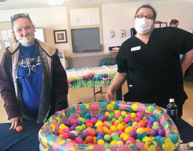 two staff members with medical face masks standing in front of easter egg ball pit
