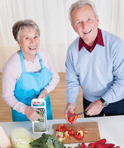 Senior couple chopping vegetables together smiling for photo