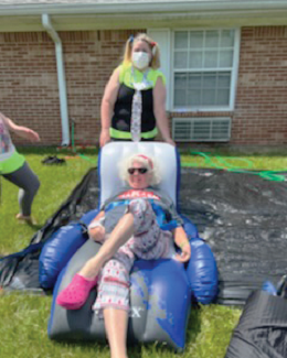 adult woman sitting in blow up recliner chair while being pushed down slip-n-slide