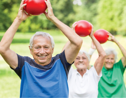 senior folks in the park exercising, holding red weighted exercise balls.