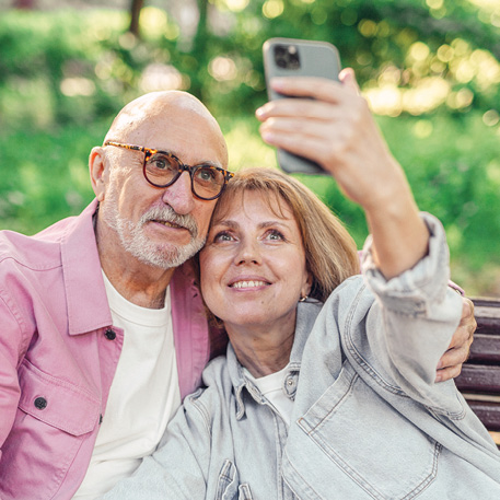 older man and woman taking a selfie on a park bench