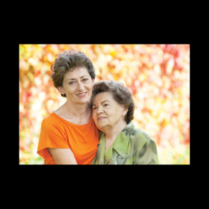 Image of senior woman in a green blouse, standing with mature daughter who is wearing an orange blouse