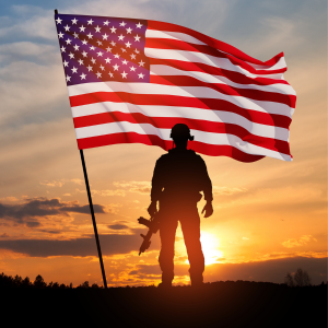 sunset image with silhouette of male solider standing next to US flag